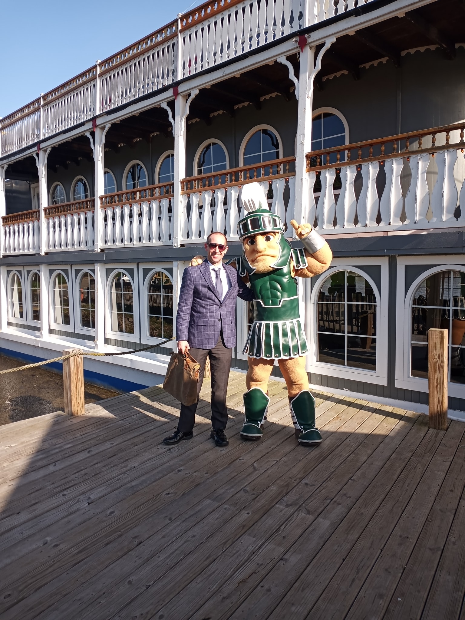 a man in a suit standing next to a Sparty in front of the Michigan Princess Riverboat
